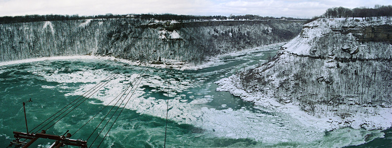 [Two images spliced together to give the expansive view of both the Niagara Gorge near the Whirlpool and the whirlpool area which is like a lake but with high walls (cliffs) around it.]